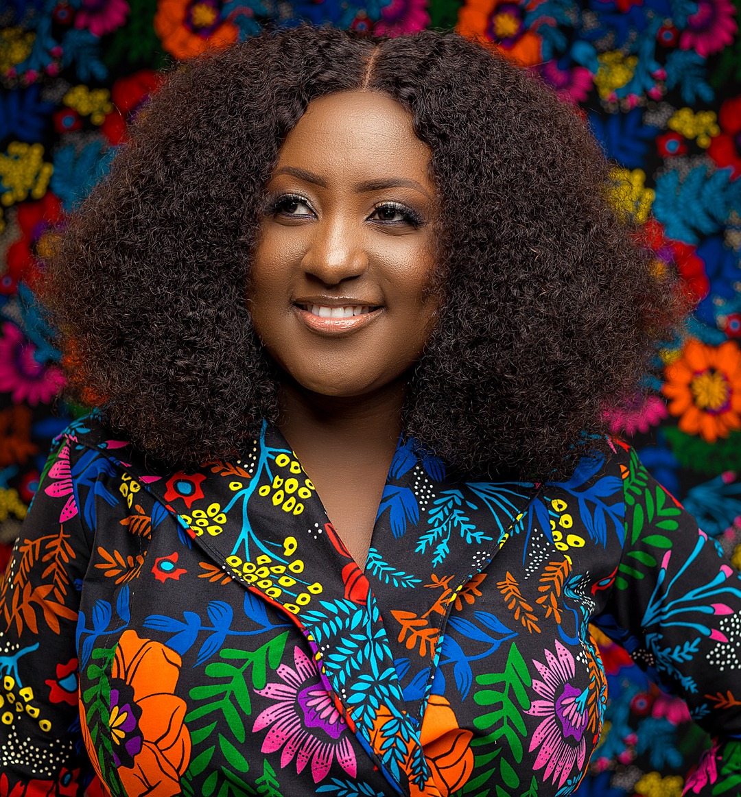 Lordina the Soprano poses with a flowery blouse that matches the background and lush hair
